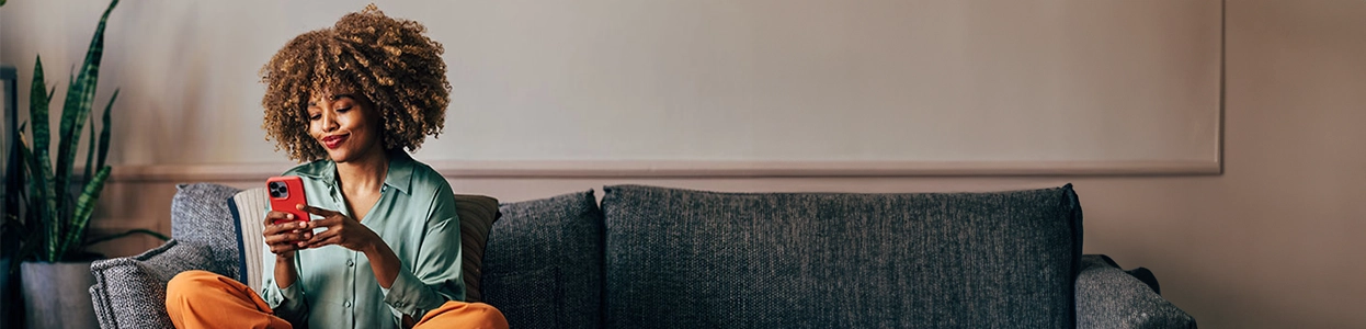 Frau sitzt entspannt auf Sofa und nutzt Smartphone