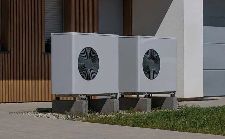 Zwei Wärmepumpen-Außengeräte auf Betonblöcken vor einem modernen Wohnhaus
