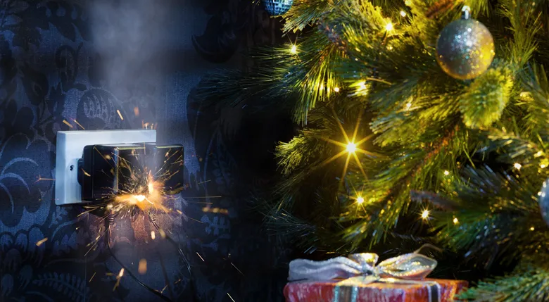 Eine Steckdose mit einem Stecker funkt und raucht gefährlich neben einem beleuchteten Weihnachtsbaum.