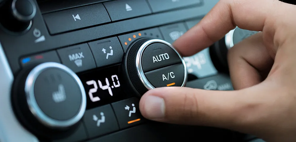 Hand dreht an der Klimaanlagen-Steuerung eines Autos, um die Temperatur auf 24 Grad einzustellen