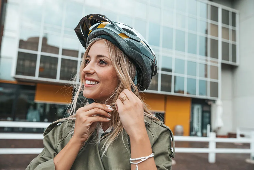 Frau setzt sich lächelnd einen Fahrradhelm auf vor einem modernen Gebäude
