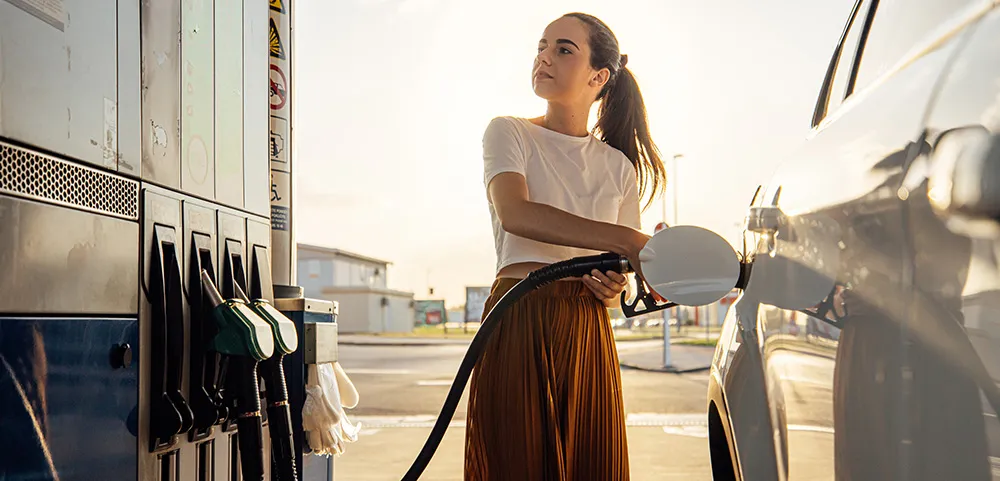 Frau tankt ihr Auto an einer Tankstelle bei Sonnenuntergang