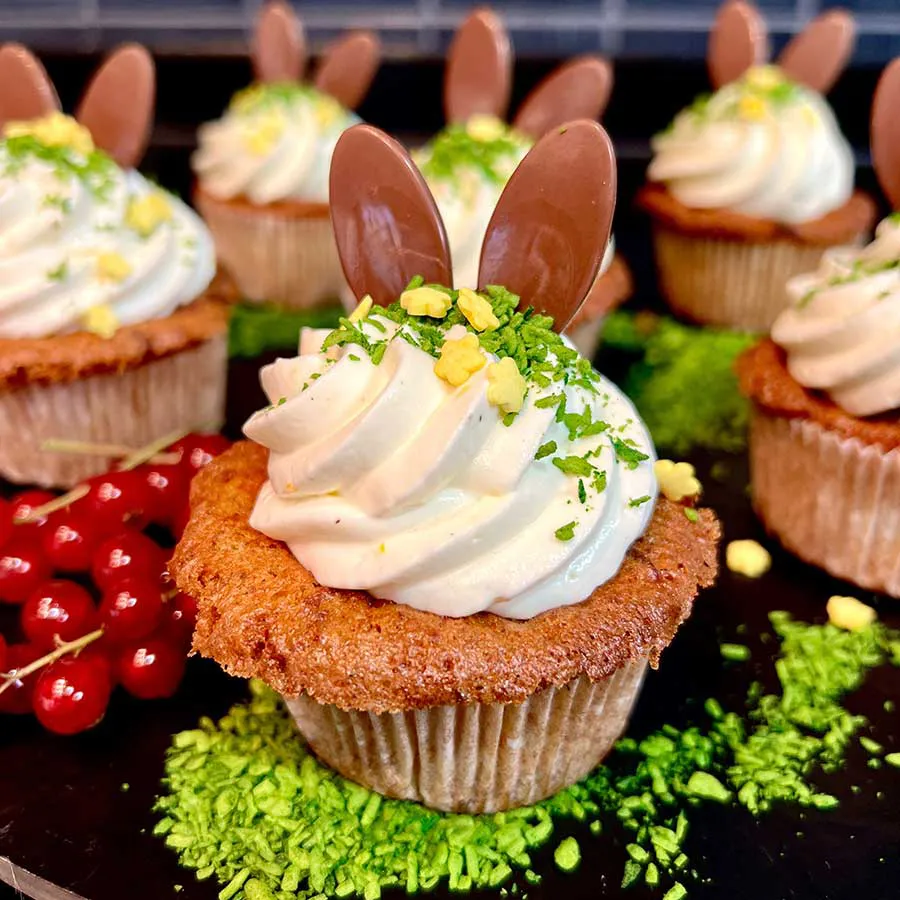 Rübli-Cupcakes mit Sahnetopping und Schoko-Ohren, dekoriert mit grünen Streuseln.