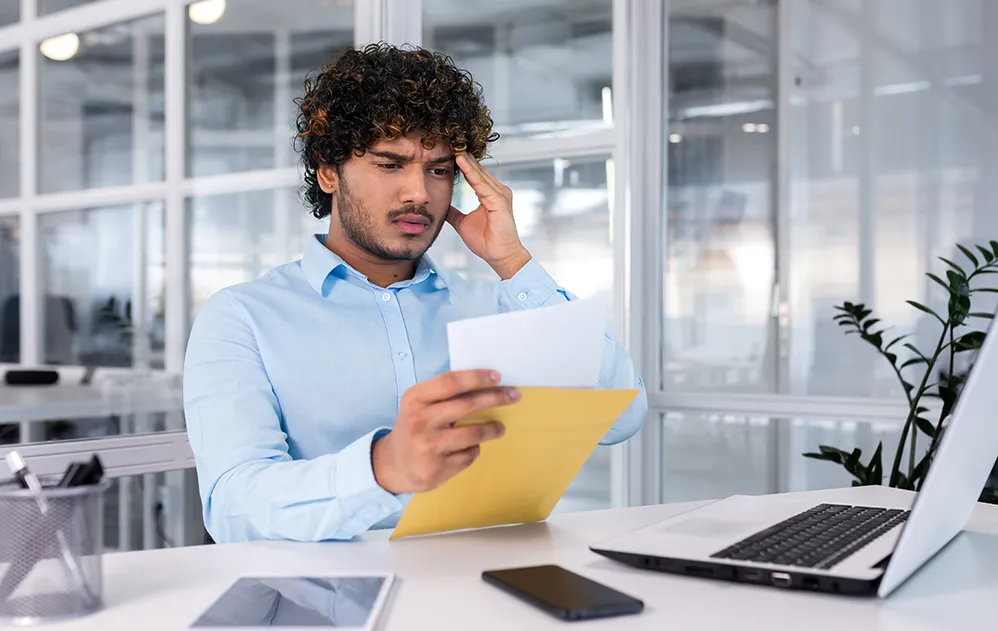 Mann sitzt im Büro und öffnet einen Brief mit einer schlechten Nachricht.