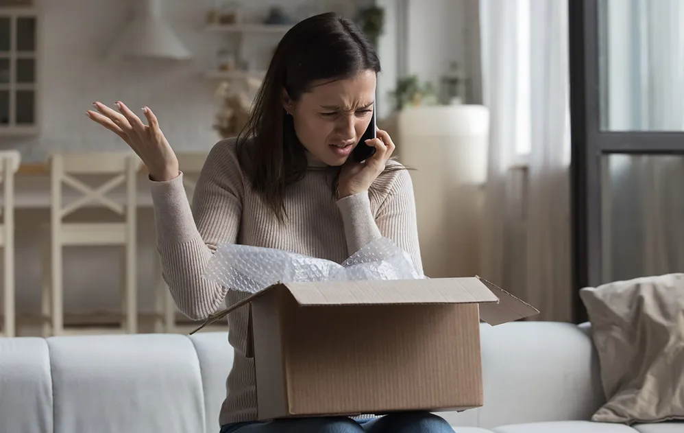 Eine Frau öffnet ein Paket und ist aufgebracht.