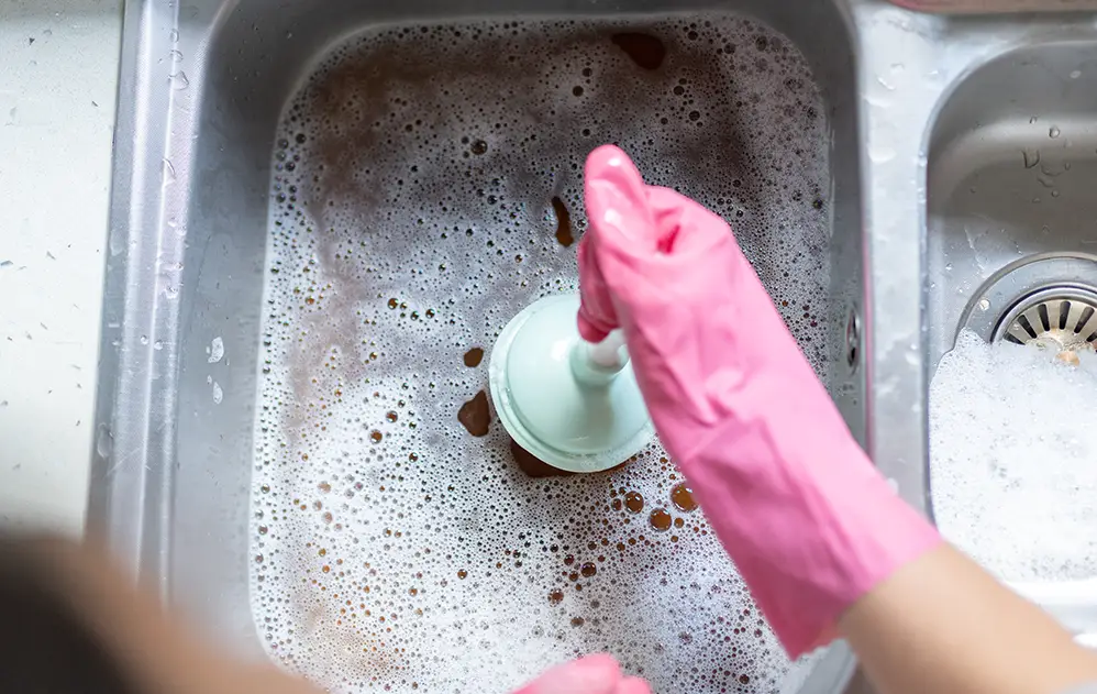 Symbolbild Rohrreinigung: Spühlbecken das verstopft ist, Person versucht Abfluss zu reinigen.