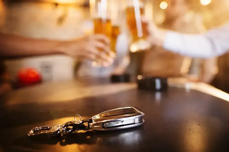 Symbolbild autofahren unter Alkoholeinfluss: Autoschlüssel liegt auf Tisch, im Hintergrund wird mit Biergläsern angestoßen.