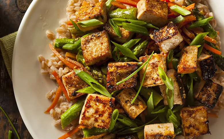 Gebratener Tofu mit Gemüse und Frühlingszwiebeln auf einem Teller.