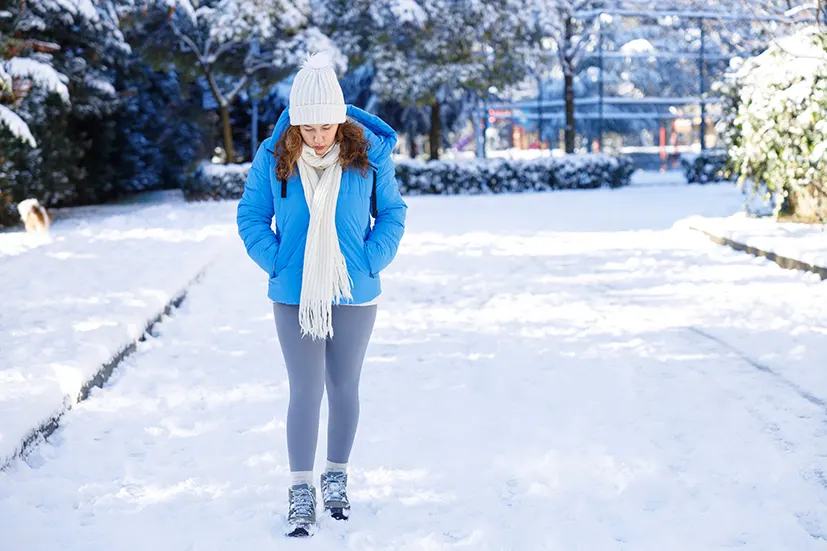 Eine junge Frau in Winterkleidung geht über eine zugeschneite Straße.