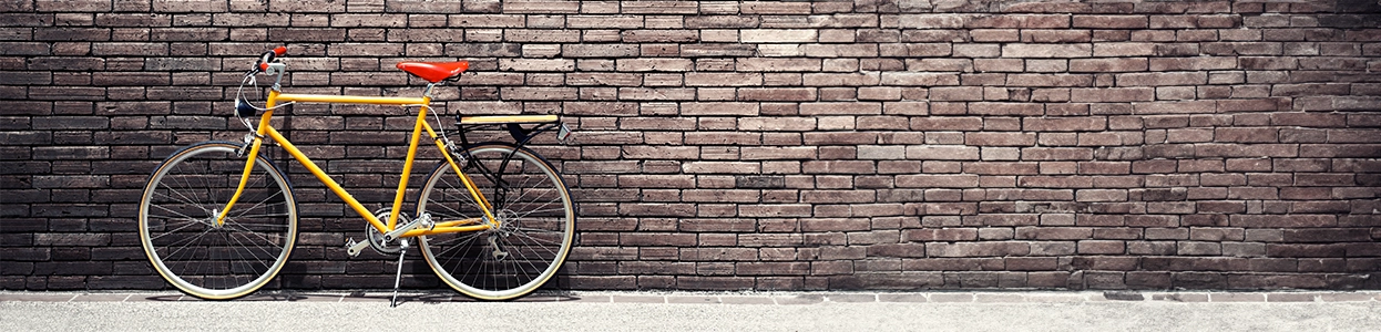 Gelbes Fahrrad mit rotem Sattel lehnt an einer Backsteinmauer