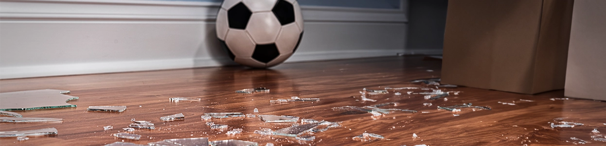 Zerbrochenes Glas auf dem Holzboden mit einem Fußball im Hintergrund