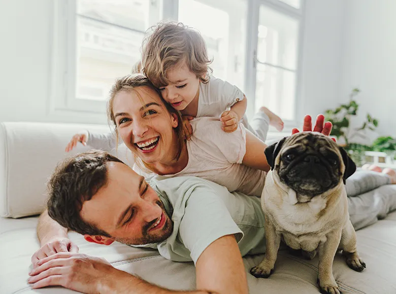 Glückliche Familie mit Kind und Hund spielt gemeinsam lachend auf dem Sofa