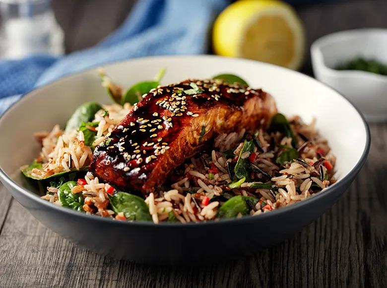 Schüssel mit gebratenem Lachsfilet in Teriyaki-Glasur auf Reis mit frischem Gemüse und Sesam