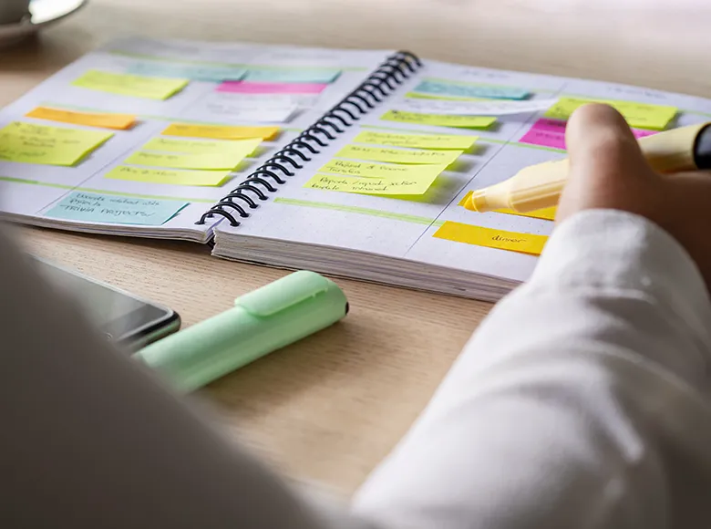 Person markiert Aufgaben in einem Planer mit bunten Post-its und Textmarkern