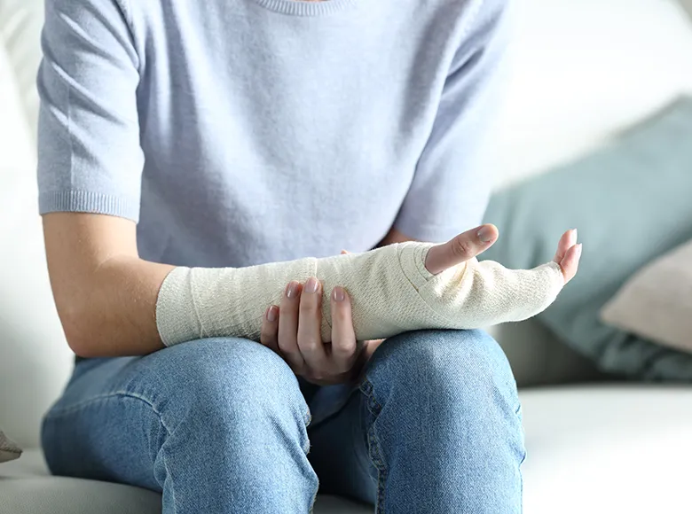 Person sitzt auf Sofa mit eingegipstem Arm und stützt ihn mit der anderen Hand
