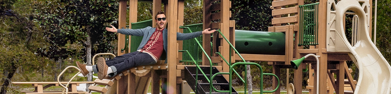 Ein fröhlicher Mann sitz auf einem Kinderspielplatz.