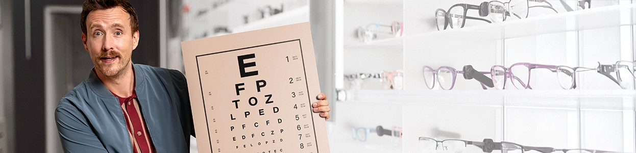 Ein freundlicher Mann hält eine Tafel mit Buchstaben beim Optiker hoch.