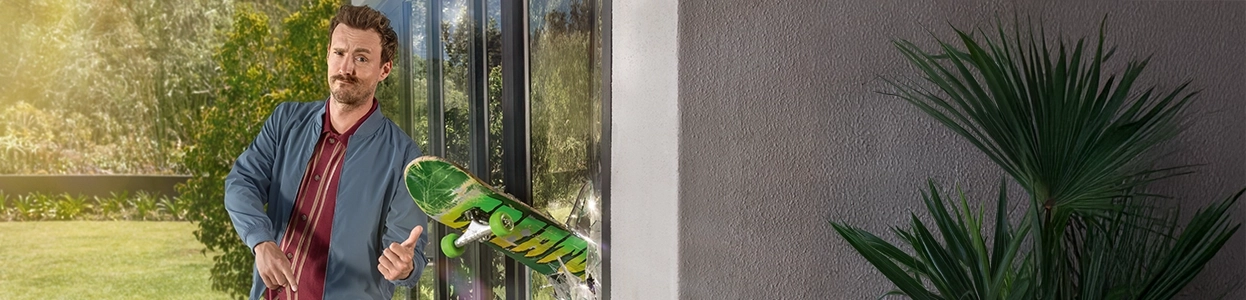 Ein Mann betrachtet kritisch ein Skateboard, dass in einem Fenster steckt.