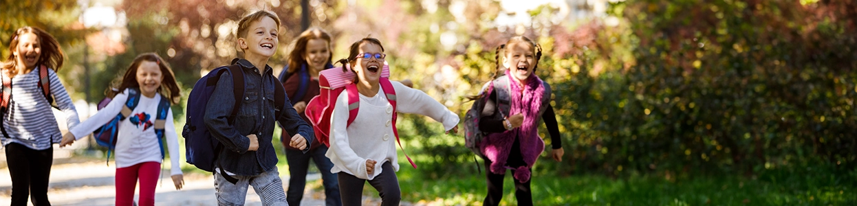 Gruppe fröhlicher Schulkinder mit Rucksäcken rennt lachend draußen auf einem Weg