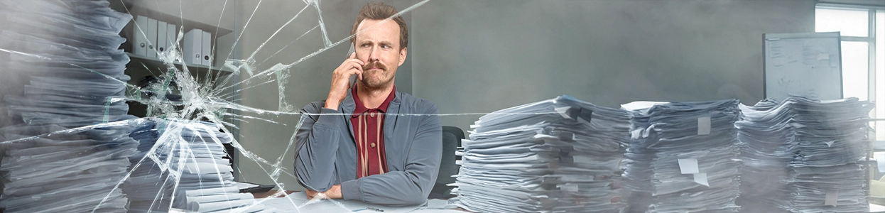 Ein kritisch schauender Mann telefoniert hinter einer gesprungenen Glasscheibe.