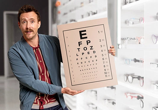 Ein freundlicher Mann hält eine Tafel mit Buchstaben beim Optiker hoch.