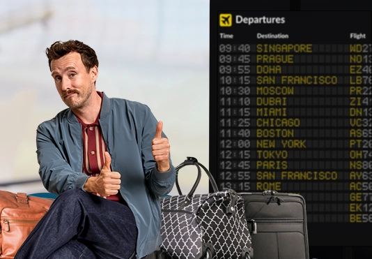 Ein freundlicher Mann sitzt auf seinen Koffern am Flughafen und zeigt zwei Daumenhoch.