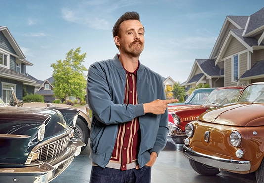 Ein freundlicher Mann zeigt stolz auf seineSammlung Oldtimer.