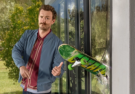 Ein Mann betrachtet kritisch ein Skateboard, dass in einem Fenster steckt.