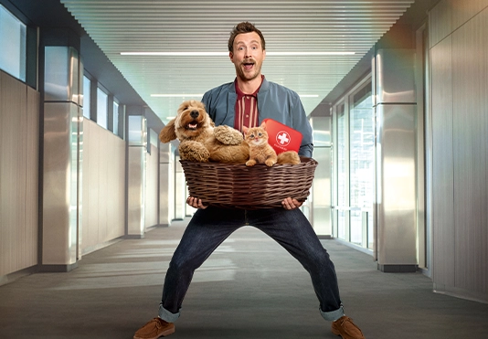 Ein begeistert guckender Mann mit einem Korb gefüllt mit einem Hund, einer Katze und einem erste Hilfe Kasten.