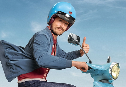 Ein lächelnder Mann auf einem Roller, der über die Straße fährt.