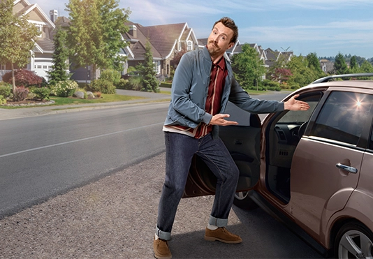 Ein freundlicher Mann deutet an, dass man auf dem Fahrersitz eines Autos Platz nehmen soll.